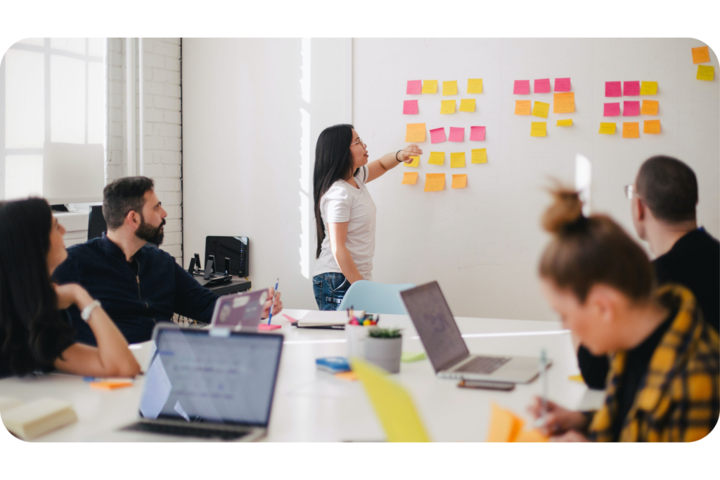 A woman explaining something to coworkers using sticky notes in a meeting - pro bono sponsors page