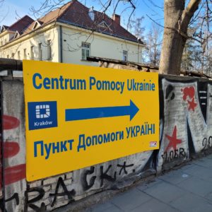 Ukraine Aid Center written in blue on a yellow sign in Polish and Ukrainian - arrow pointing right