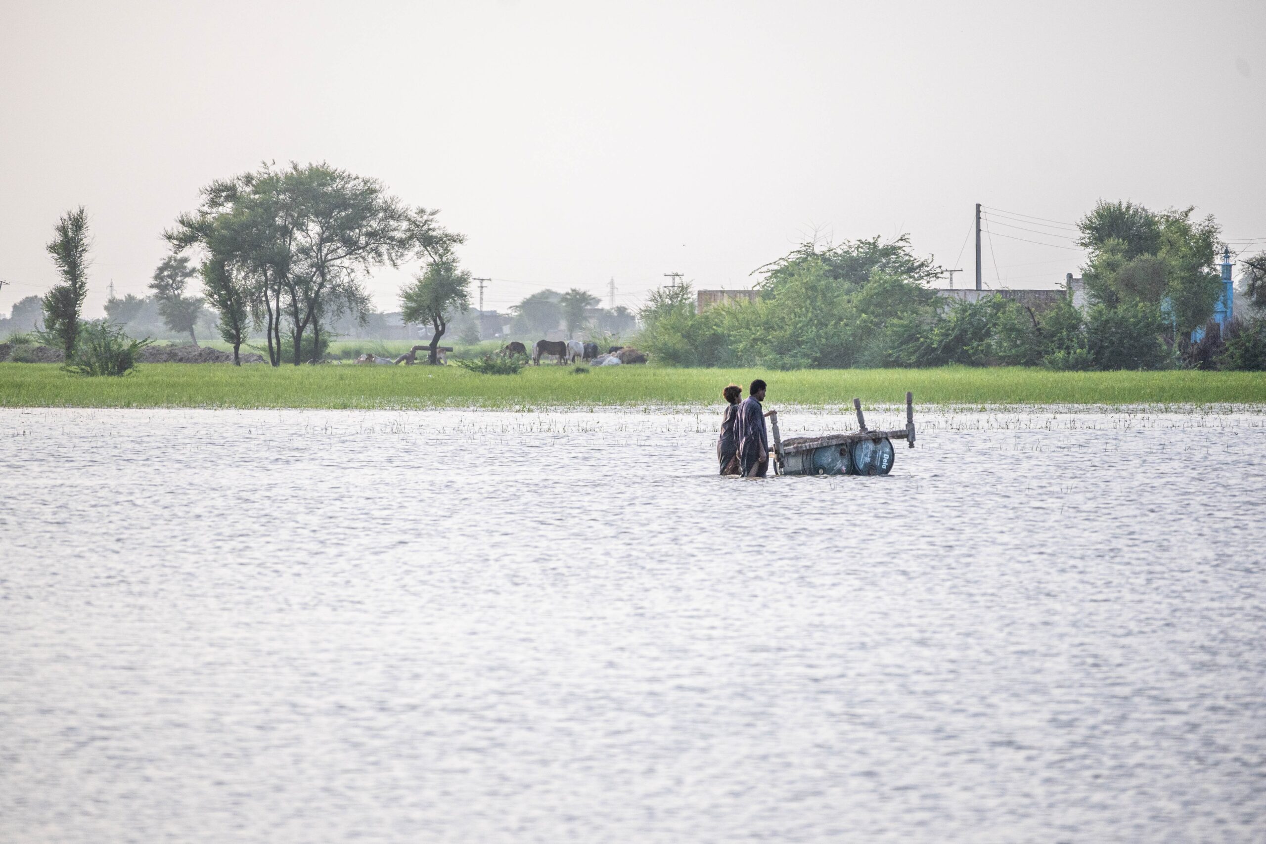 Photo of two people standing in flood waters, with a town in the background, Pakistan.