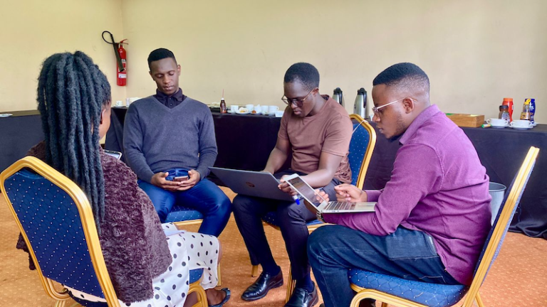 Reach A Hand Uganda workshop - contributors sat in a circle reviewing our Language AI Playbook.
