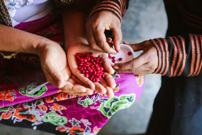 Close up of a Rohingya woman and child holding red beans in their hands, wearing colorful clothes