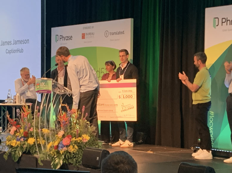 An image of James Jameson, CEO of CaptionHub giving a speech at LocWorld 51 with two people standing behind holding a big sized cheque.