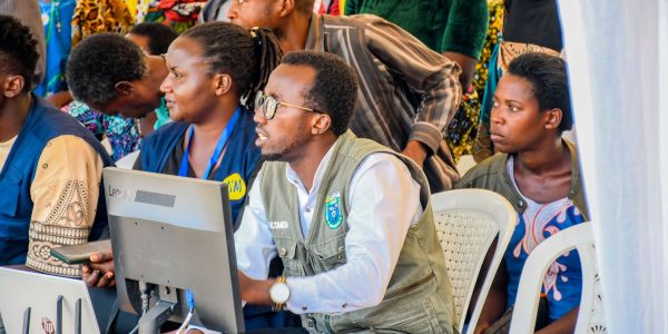 A diverse group of adults engaging with technology at a community event in Rwanda.