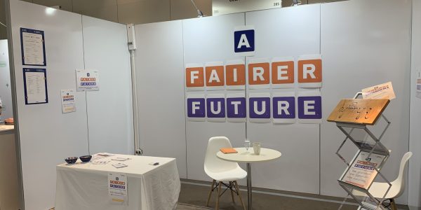 Image of a white booth with the words "a fairer future" written on paper tiles in orange and purple